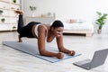 Plus size Afro lady working out at home with online personal trainer, using laptop, standing in elbow plank pose Royalty Free Stock Photo