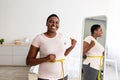 Plus size black woman measuring waist with tape in front of mirror, showing results of slimming diet, gesturing thumb up Royalty Free Stock Photo