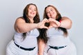 Plus size caucasian sisters woman wearing casual white clothes smiling in love doing heart symbol shape with hands Royalty Free Stock Photo