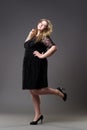 Plus size fashion model in black dress, fat woman on gray background Royalty Free Stock Photo