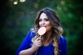 Plus size fashion model in blue dress outdoors, beauty woman licks lollipop, professional makeup and hairstyle Royalty Free Stock Photo