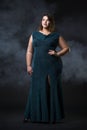 Plus size fashion model in green evening dress, fat woman on black background, overweight female body