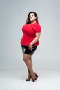 Plus size fashion model in red blouse and black skirt, fat woman on gray background, body positive concept Royalty Free Stock Photo