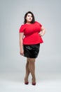 Plus size fashion model in red blouse and black skirt, fat woman on gray background, body positive concept Royalty Free Stock Photo