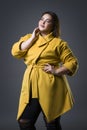 Plus size fashion model in yellow coat and black hat, fat woman on gray background, overweight female body Royalty Free Stock Photo