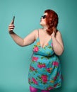 Plus-size fat woman in fashion sunglasses and colorful sundress does fashion selfie on mint