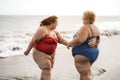 Plus size friends walking on the beach having fun during summer vacation - Focus on right woman back Royalty Free Stock Photo