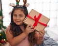 Plus size hispanic girl hearing gift sound standing by christmas tree at home