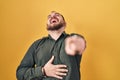 Plus size hispanic man with beard standing over yellow background laughing at you, pointing finger to the camera with hand over Royalty Free Stock Photo