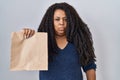 Plus size hispanic woman holding take away paper bag thinking attitude and sober expression looking self confident