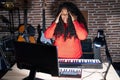 Plus size hispanic woman playing piano at music studio with hand on head for pain in head because stress