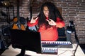 Plus size hispanic woman playing piano at music studio shouting with crazy expression doing rock symbol with hands up