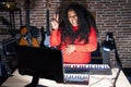 Plus size hispanic woman playing piano at music studio smiling with happy face winking at the camera doing victory sign