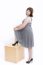 Plus size model in gray dress and heels on white background. Overweight young woman standing on a wooden box Royalty Free Stock Photo