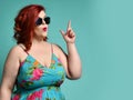 Plus-size overweight lady in sunglasses and sundress point her finger up like she has got an idea at free text copy space on mint