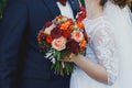 Plus size wedding couple is standing and hugging outside. Curvy bride is holding beautiful colorful bouquet with orange, red and Royalty Free Stock Photo