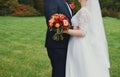 Plus size wedding couple is standing and hugging outside. Curvy bride is holding beautiful colorful bouquet with orange, red and Royalty Free Stock Photo