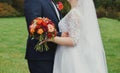 Plus size wedding couple is standing and hugging outside. Curvy bride is holding beautiful colorful bouquet with orange, red and Royalty Free Stock Photo