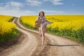 Plus size woman in floral dress, barefoot, on a road between canola fields Royalty Free Stock Photo