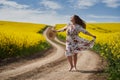 Plus size woman in floral dress, barefoot, on a road between canola fields Royalty Free Stock Photo