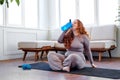 plus size woman with red hair siit on fitness mat drinking water, training at home Royalty Free Stock Photo