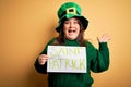 Plus size woman wearing green hat celebrating st patricks day holding saint patricks day banner very happy and excited, winner