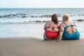 Plus size women sitting on the beach having fun during summer vacation - Rear view of curvy female laughing together - Overweight Royalty Free Stock Photo