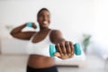 Plus size young black woman doing exercises with dumbbells, strengthening her body at home, selective focus