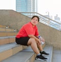 Plus size young woman sitting  down on stairs with bottle of fresh water in hand and taking a break from city outdoors exercising Royalty Free Stock Photo