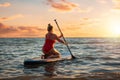 Plus sized beautiful Caucasian woman in red swimsuit swimming sitting on a sup board. Sunset on the background. Back Royalty Free Stock Photo