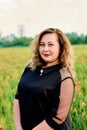 Plus sized woman in a black dress on a field of green wheat and wild poppies. Overweight fat woman