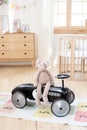 Plush rabbit is sitting in a black vintage racing children`s car in a children`s room. The interior of the kindergarten room. Retr