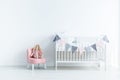 Plush toy on pink chair next to white crib in white baby`s bedro