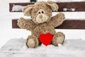 Plush toy with a red heart on a snow-covered bench. Valentine`s Day. Holiday gift. Love confession concept Royalty Free Stock Photo