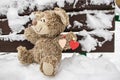 Plush toy with a red heart on a snow-covered bench. Valentine`s Day. Holiday gift. Love confession concept Royalty Free Stock Photo