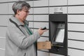 Senior woman with smartphone entering code to open shopping locker in inPost delivery service for receives or sends box. Royalty Free Stock Photo