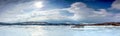 Panorama of frozen lake with small island in Northern Mountains starting to melt and water flows on the ice surface. Blue skies Royalty Free Stock Photo