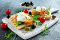 Poached egg on grilled toast with smoked salmon, rucola, olives and vegetables on white board. healthy breakfast