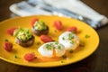 Poached eggs with avocado stuffed mushrooms, tomatoes, and green onions on a cheery yellow plate