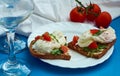 Poached eggs on sandwich of rye bread with sauce, tomatoes and arugula in white plate on blue background.