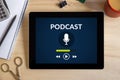 Podcast concept on tablet screen with office objects on wooden d