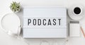 Podcast word on lightbox with headphones, coffee cup and notepad on white table