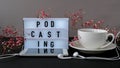 Podcasting lettering. Headphones mobile phone. Dry pink flowers decoration. Workplace. Black coffee