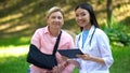 Podiatric physician with tablet and elderly woman in arm sling smiling on camera