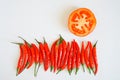 Pods of red chili peppers and half a tomato lie on a white surface. Seasoning and healthy food. Free space for inscriptions