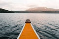 pointed bow of a white and orange wooden kayak heading to the leafy island navigating the waves of the lake at sunset