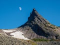 Pointed cliff with a small snow glacier, moon in the blue evening sky. Awesome scenic mountain landscape with big pointed stones