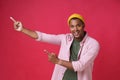 Pointing, gesturing with two hands sideways left young african american man wearing pink shirt, khaki, green t-shirt and yellow Royalty Free Stock Photo