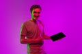 Studio image of young caucasian man with digital tablet on pink background in neon light. Concept of emotions, youth Royalty Free Stock Photo