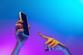 Closeup female hands holding gadget, smartphone on gradient blue and purple background in neon. Concept of